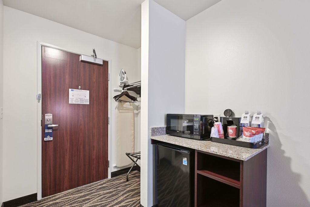 A compact hotel room with a kitchenette featuring a microwave, coffee maker, and a refrigerator.
