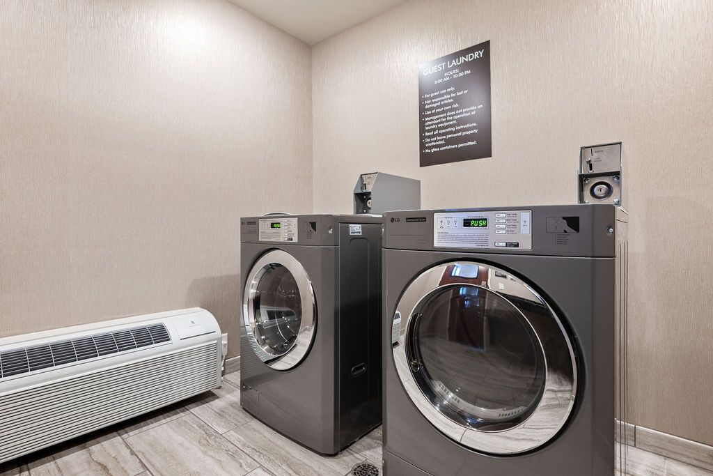 A hotel laundry room with two front-loading washers and a wall-mounted dryer.