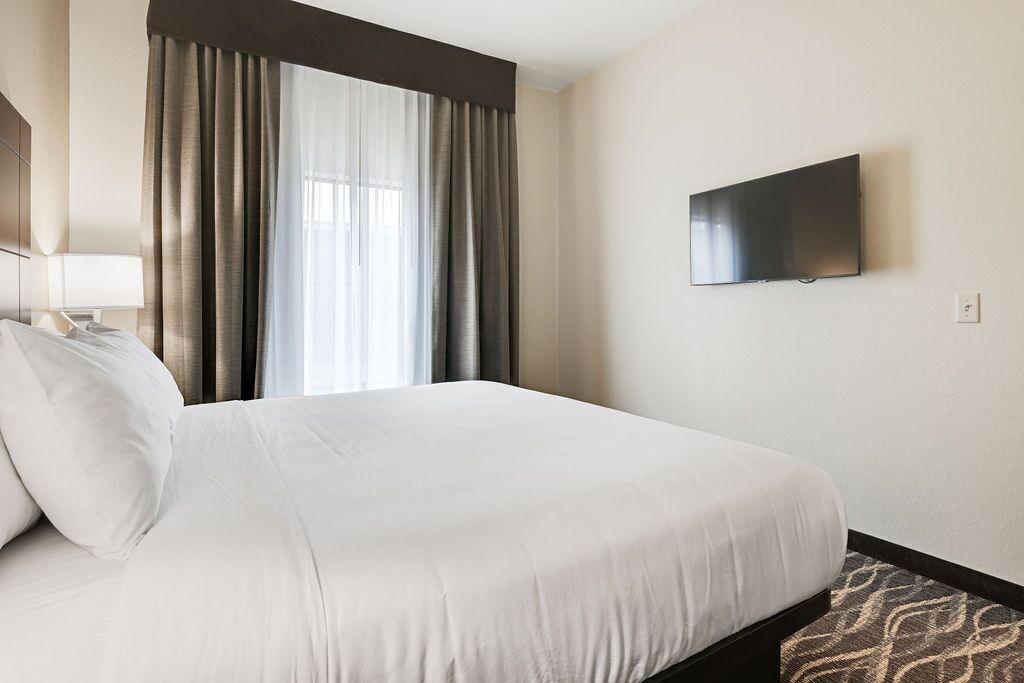 A hotel room with a large bed, a flat-screen TV mounted on the wall, and a window with curtains.