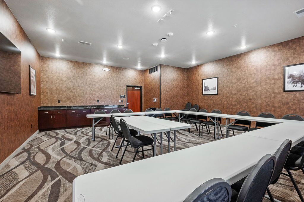 A conference room with a long table, chairs, a kitchenette, and a patterned carpet.