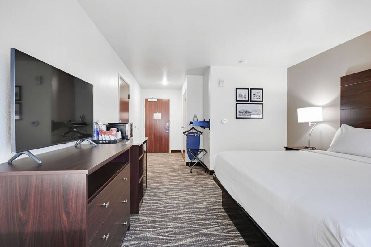 Une chambre d’hôtel comprenant un lit, une télévision, une commode, un miroir et une porte donnant sur une autre pièce.