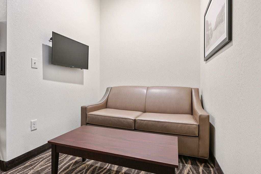 A room with a beige leather sofa, a flat-screen TV mounted on the wall, and a wooden coffee table.