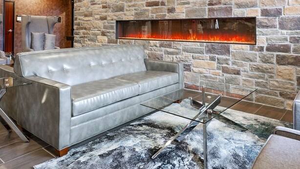 A modern living room with a stone wall, a fireplace, a leather sofa, and a glass coffee table. - Cobblestone Hotel & Suites - Central Wisconsin Airport (Mosinee)