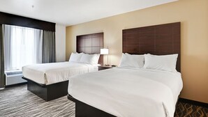 A hotel room with two beds, a large window with curtains, a wall-mounted headboard, and a bedside table with a lamp. - Cobblestone Hotel & Suites - Central Wisconsin Airport (Mosinee)