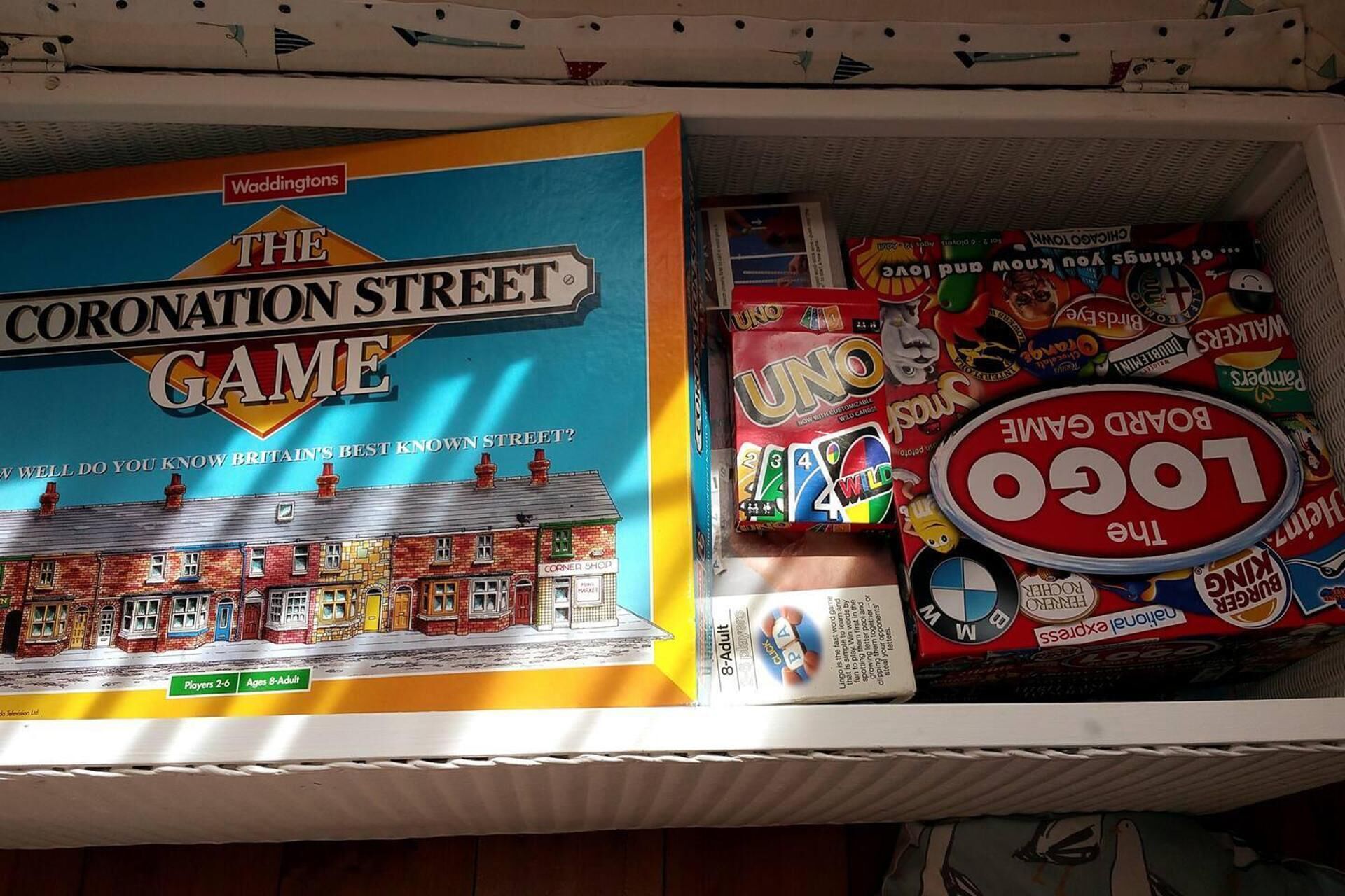 Una estantería con juegos de mesa, incluyendo 'The Coronation Street Game' y 'Uno'.