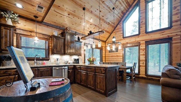 Een knus chaletinterieur met houten wanden, een keuken met houten kastjes, een eethoek met tafel en stoelen, en een groot raam dat natuurlijk licht binnenlaat.