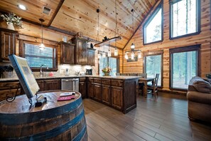 L’intérieur d’un chalet rustique, avec des murs en bois, une cuisine dotée de meubles en bois, un coin repas avec une table et des chaises, et une grande fenêtre laissant entrer la lumière naturelle.