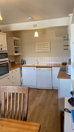 Cozinha compacta com armários brancos, uma lava-louças e uma mesa de jantar de madeira.