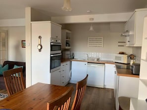 Uma cozinha compacta com armários brancos, micro-ondas, lava-louças e uma mesa de jantar de madeira com cadeiras.