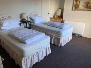 A room with two single beds, a wooden dresser, a lamp, and a radiator.