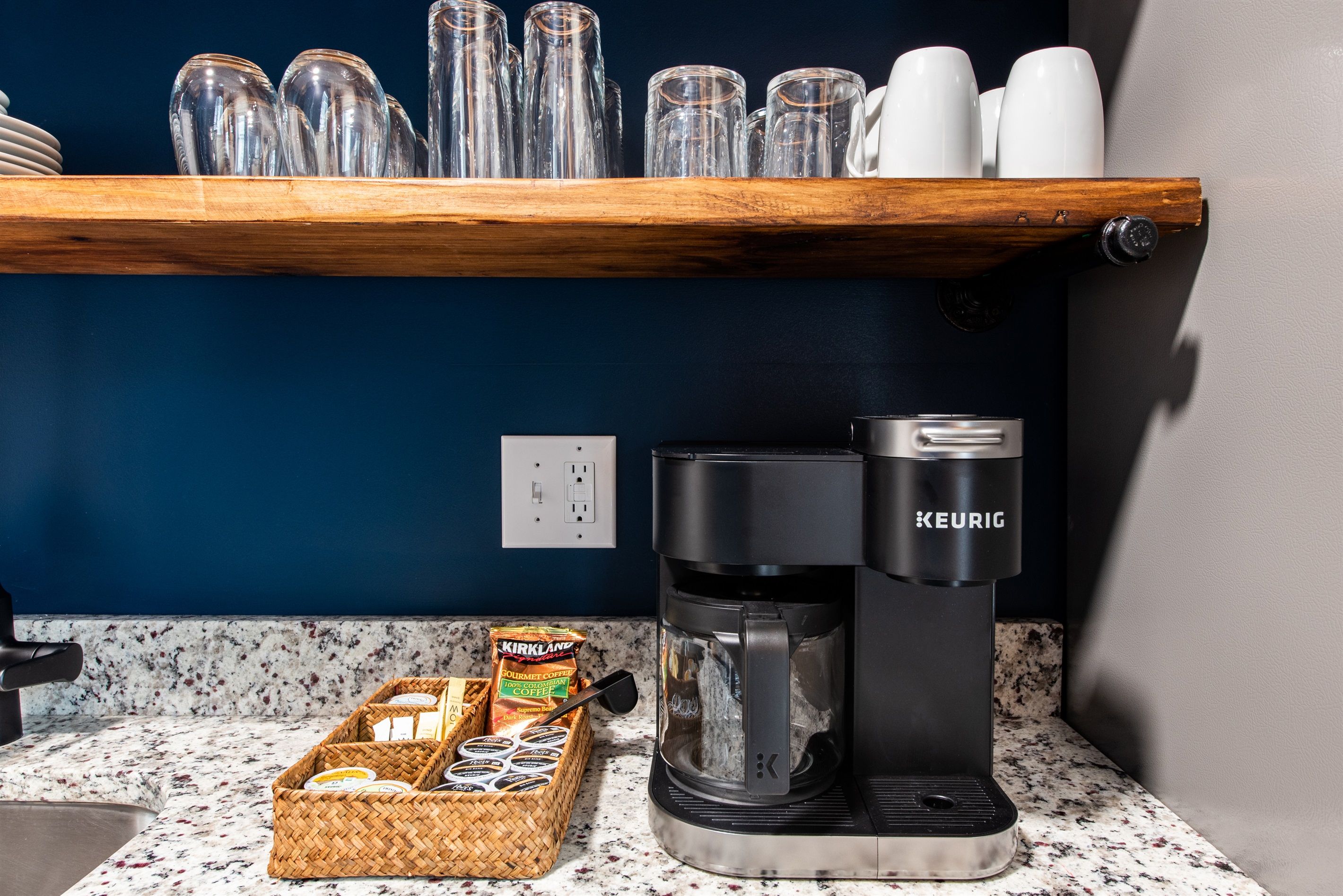 A coffee station with a Keurig coffee maker, a basket of coffee pods, and a container of coffee mugs.