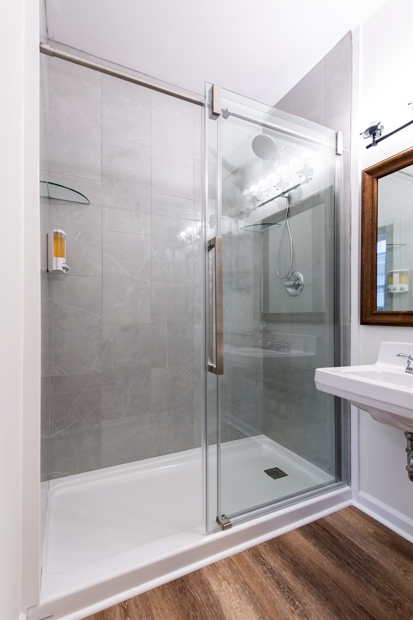 Une salle de bain moderne avec une douche à parois de verre, un lavabo blanc et un plancher en bois.