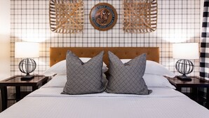 A hotel room with a plaid wallpaper, a wooden headboard, two nightstands with lamps, and a bed with patterned pillows.