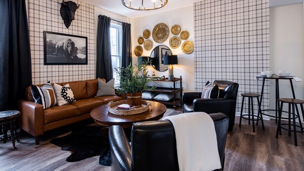 Un salon avec un canapé en cuir marron, des fauteuils en cuir noir, une table basse en bois et un lustre.