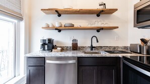 Una cocina moderna con armarios oscuros, un lavavajillas de acero inoxidable, un lavamanos doble y estantes de madera sobre la encimera.