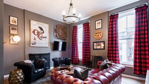 Una sala de estar con un sofá de cuero rojo, sillones de cuero negro, una chimenea y cortinas a cuadros rojos y negros.