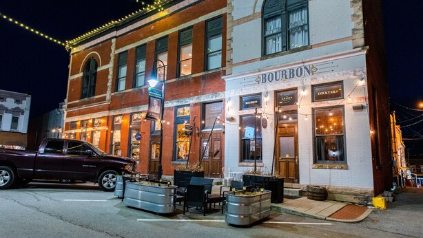 Un edificio histórico con un bar llamado 'BOURBON' en la planta baja, que cuenta con terraza al aire libre y una fachada clásica de ladrillo.