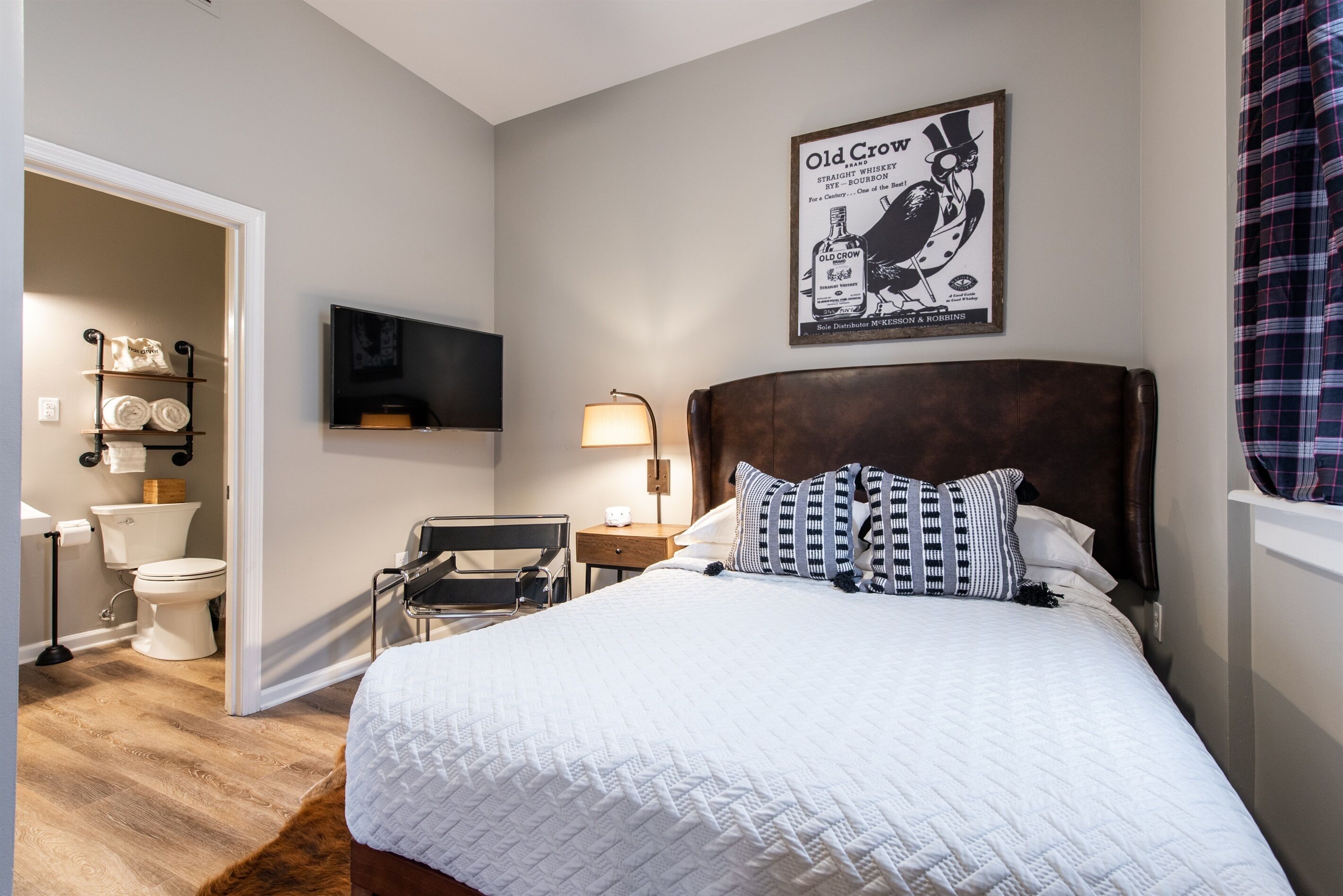 A bedroom with a large bed, a wooden headboard, a flat-screen TV mounted on the wall, a bedside table with a lamp, and a poster of a bird on the wall.