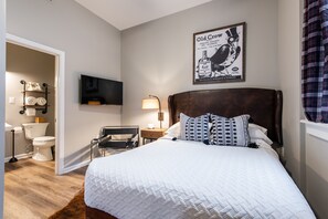 Un dormitorio con una cama grande, cabecera de madera, televisor de pantalla plana en la pared, mesita de noche con lámpara y un cartel con un pájaro en la pared.