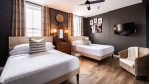 Ein Hotelzimmer mit zwei Betten, einem Fernseher, einem Deckenventilator, einem Holzschrank und einem Korbstuhl.