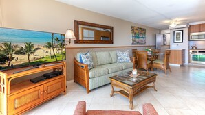 Een woonkamer met een televisie, bank, stoelen en een eethoek met een tafel en stoelen.