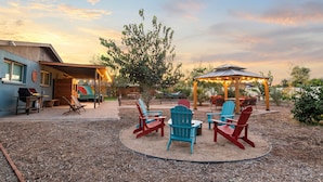 Un espace extérieur aménagé avec une terrasse, des fauteuils Adirondack, un coin salon abrité et un barbecue.