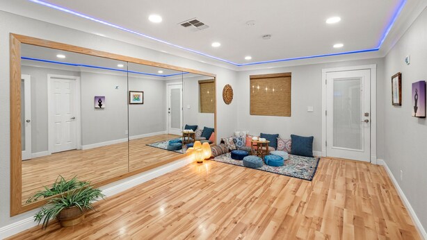 Une pièce spacieuse dotée d’un grand miroir, d’un parquet et d’un coin salon avec des coussins et une petite table.