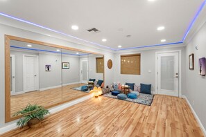 Una habitación amplia con un espejo grande, suelo de madera y un rincón de descanso con cojines y una mesita.