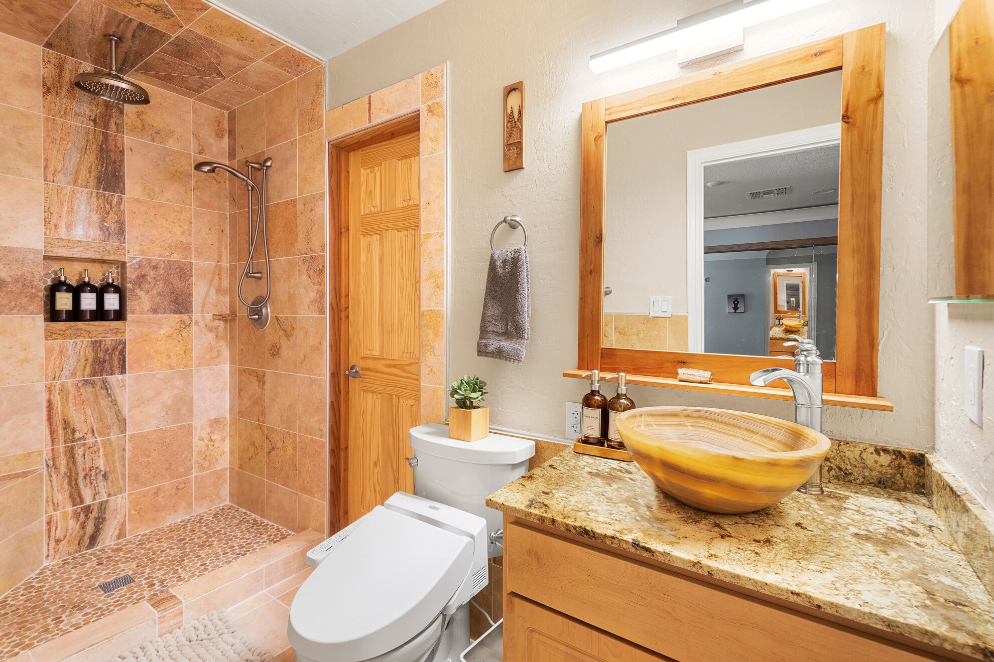Baño con ducha, inodoro, lavamanos y espejo.