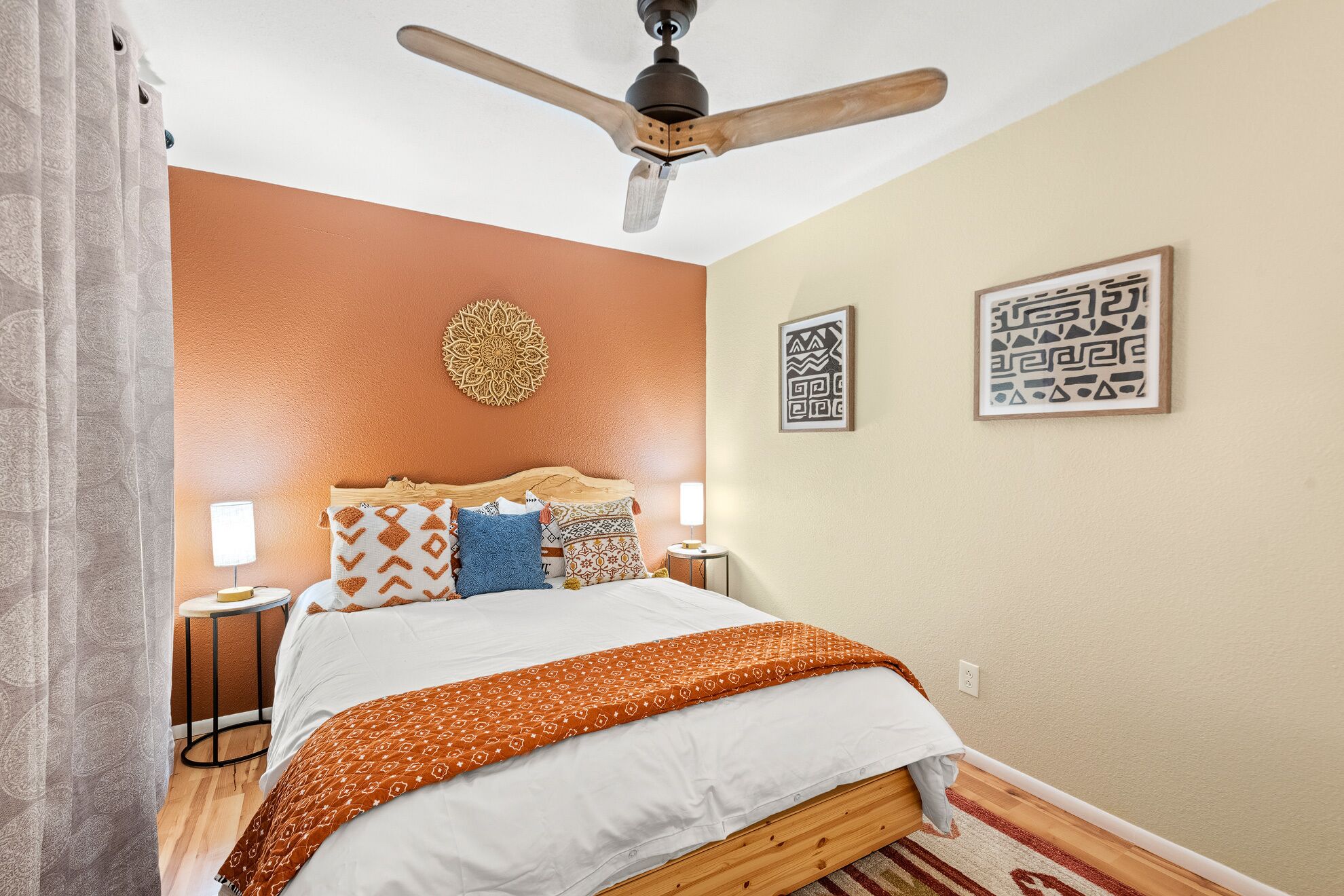 A bedroom with a wooden bed, patterned pillows, a ceiling fan, and decorative wall art.
