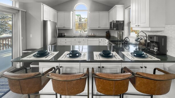 Una cocina moderna con armarios blancos, una isla grande con taburetes y vistas al exterior.