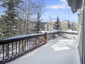 Une terrasse enneigée, dotée d’une rambarde en bois, d’une table et de chaises.