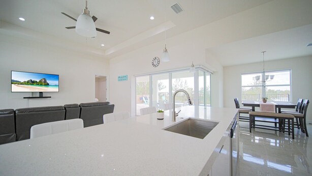 A modern kitchen with a large island, a dining area with a table and chairs, a built-in oven, and a television mounted on the wall.