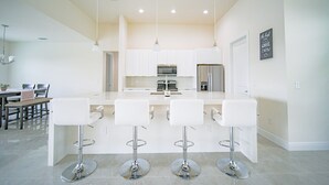 A modern kitchen with white cabinets, a central island with bar stools, stainless steel appliances, and pendant lighting.