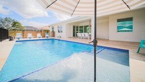 A swimming pool with a striped umbrella, lounge chairs, and a patio area with a view of the sky.