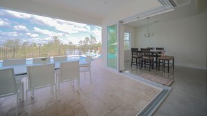 A spacious room with a large sliding glass door leading to a pool area, a dining table with chairs, and a chandelier.