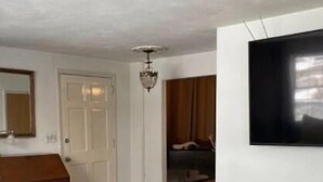 A room with a wooden bench, a television mounted on the wall, a door, and a dresser.