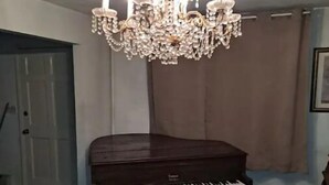 A grand piano in a room with a chandelier and a door in the background.