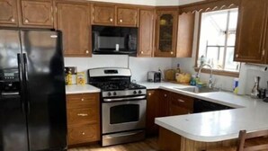 A kitchen with wooden cabinets, a black refrigerator, a stove, and a trash bin.