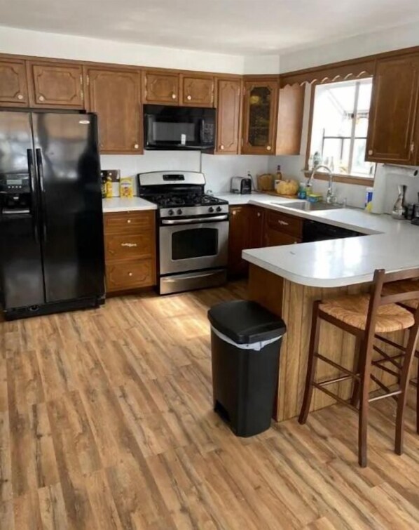 A kitchen with wooden cabinets, a black refrigerator, a stove, and a trash bin.