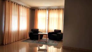 A living room with two sofas, a coffee table, and a large window with curtains. - Home away from Home -Beautiful and Spacious House (katabi, Entebbe)
