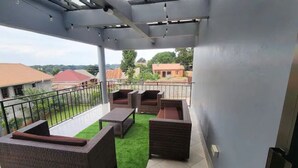 A covered balcony with wicker furniture, a green artificial turf, and a view of surrounding buildings. - Home away from Home -Beautiful and Spacious House (katabi, Entebbe)