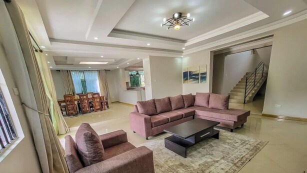 A spacious living room with a sectional sofa, a coffee table, and a patterned rug. - Home away from Home -Beautiful and Spacious House (katabi, Entebbe)