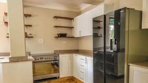 A kitchen with white cabinets, a stainless steel refrigerator, and a wood-burning stove. - Home away from Home -Beautiful and Spacious House (katabi, Entebbe)
