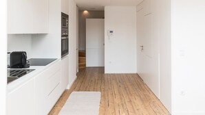 Un pasillo estrecho con armarios blancos, una zona de cocina con electrodomésticos y suelo de madera.