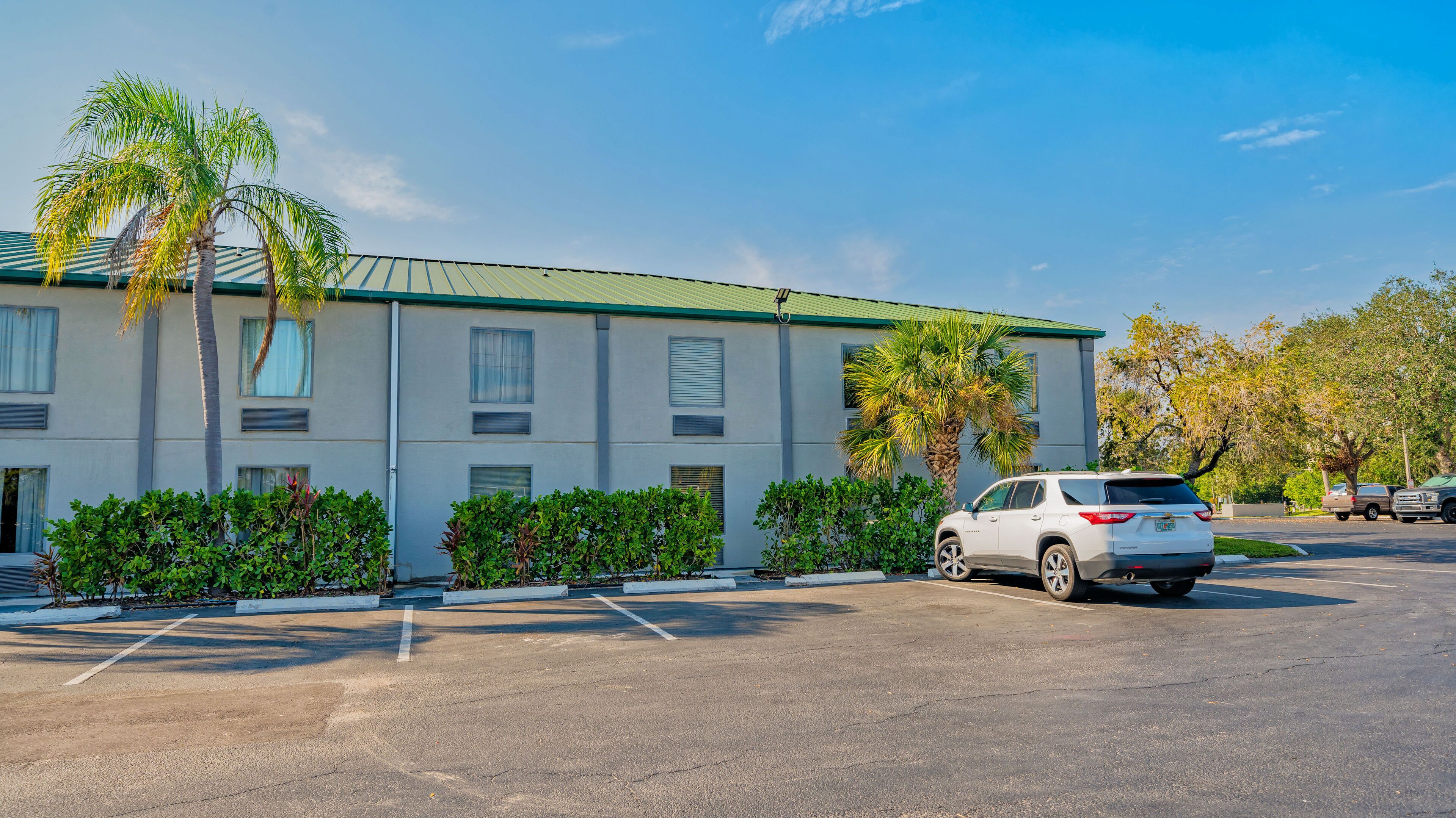 A motel with a parking lot, a white SUV parked, and palm trees.