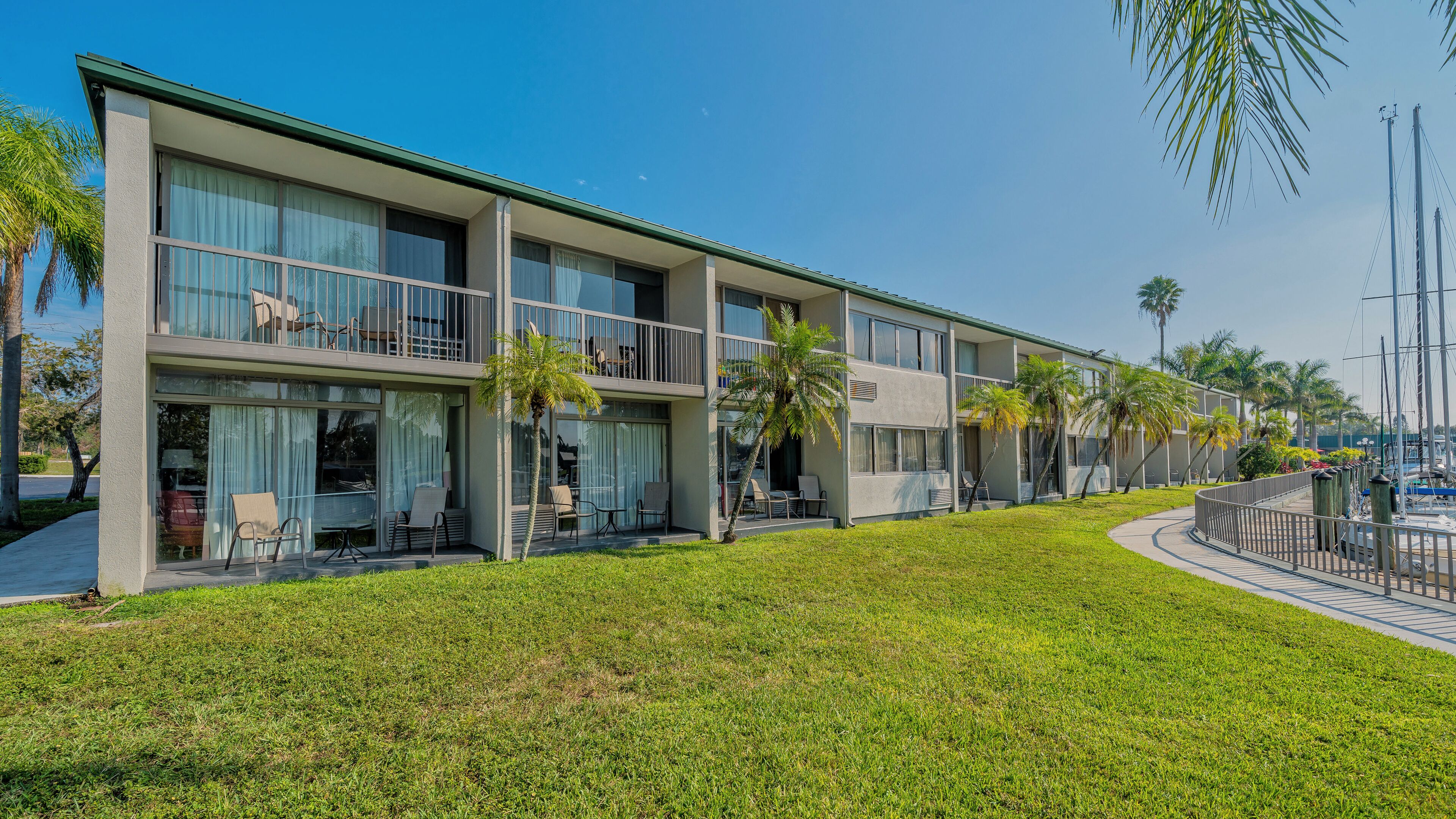A modern multi-story hotel with balconies, outdoor seating, and a well-maintained lawn.