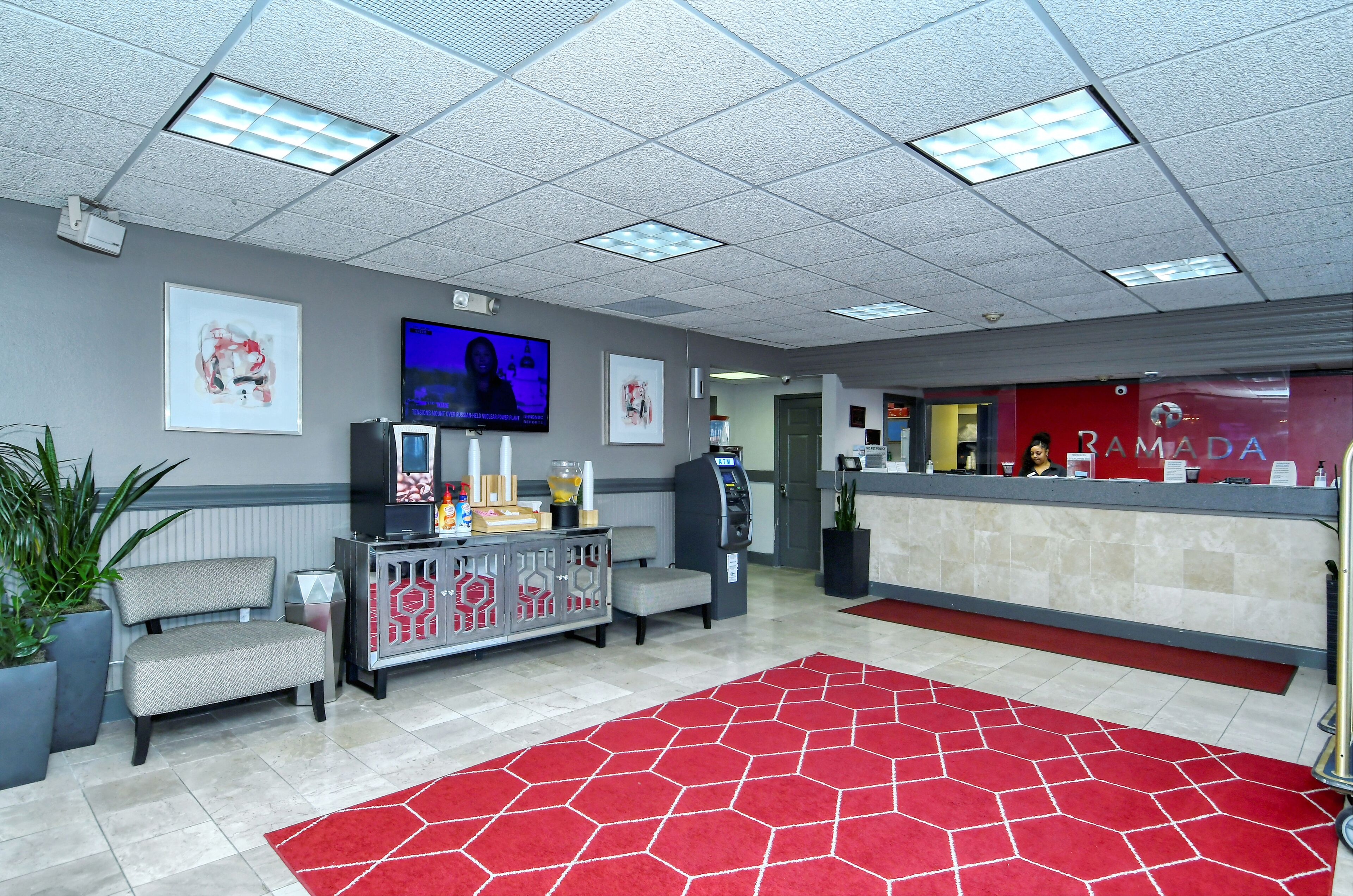 A hotel reception area with a red carpet, a reception desk, a television, and a vending machine.