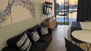 A modern living room with a sofa, a dining table, and a view of a body of water through large windows. - ALL-NEW Waterfront Room, Heated Pool, Tiki Bar/Grill (Sarasota)