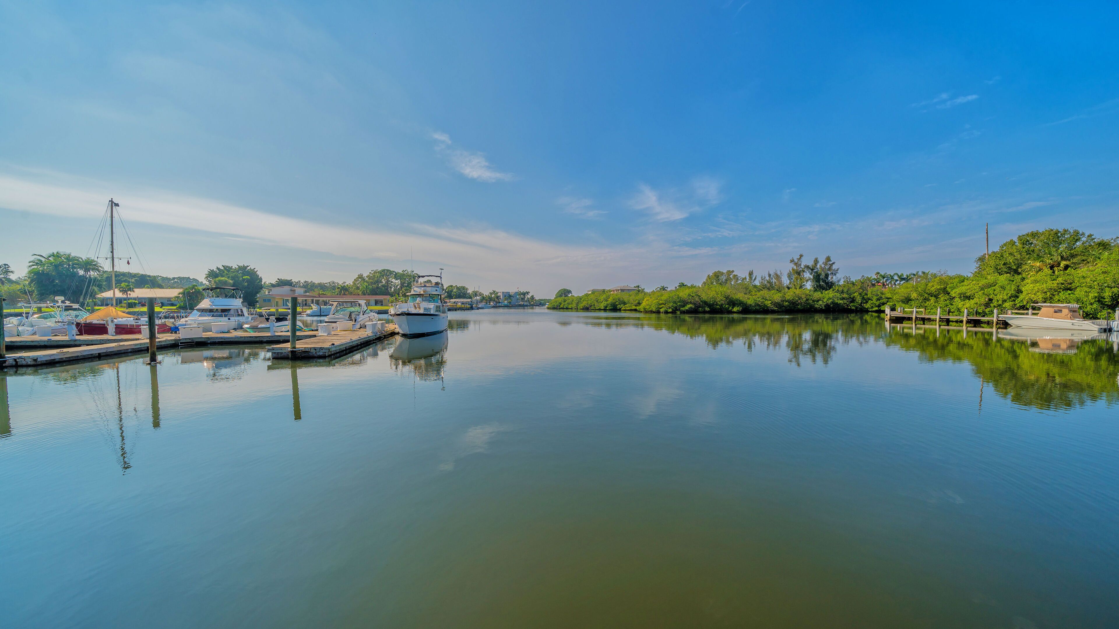 A marina with boats docked, calm water, and greenery in the background.